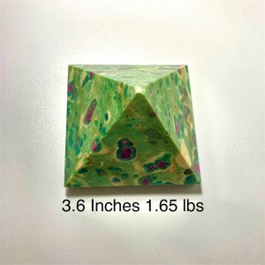 May include: A green and red pyramid-shaped decorative object. The pyramid is 3.6 inches tall and weighs 1.65 pounds. The pyramid has a speckled pattern of green and red throughout its surface. The object is sitting on a white surface.