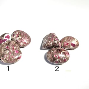 May include: Two groups of tumbled stones, each with a unique arrangement. The stones are a mix of white, gray, and dark pink. The pink appears in patches and speckles, creating a speckled effect. The stones have a smooth, rounded shape.