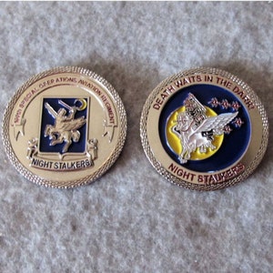 May include: A silver coin with a blue and yellow design featuring a winged horse and the text "Death Waits in the Dark!" and "Night Stalkers". The other side of the coin features a crest with a winged horse and the text "160th Special Operations Aviation Regiment" and "Night Stalkers".
