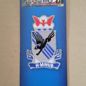 May include: Embroidered patch with a shield design featuring a black bird in flight, blue stripes, and the text "H-MINUS". The patch has a red and white top design and is on a blue background.