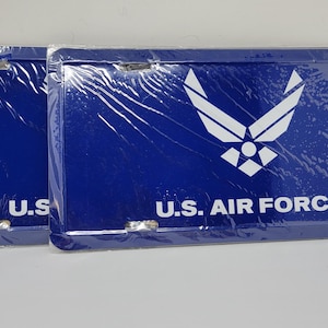 May include: Two blue license plates with the text "U.S. AIR FORCE" and a white Air Force emblem. The plates are rectangular with rounded corners and are wrapped in clear plastic.