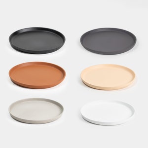 May include: Six round trays in different colors. The trays are made of a textured material and are perfect for serving snacks or drinks. The colors are black, gray, brown, beige, gray with white flecks, and white.
