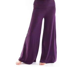 May include: A woman wearing a purple tank top and wide-legged pants. She is wearing a gold necklace with a pendant.