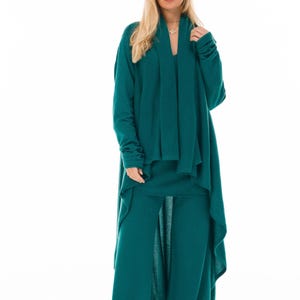Può includere: Un completo verde teal composto da tre pezzi: un cardigan lungo con drappeggio frontale, un top e pantaloni a gamba larga con spacco. L'outfit è realizzato in un tessuto morbido e fluido.