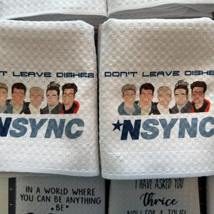 May include: White kitchen towels with a black and blue graphic of the boy band *NSYNC. The text on the towels reads "Don't Leave Dishes".