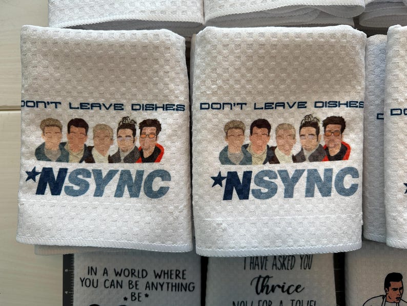 May include: White kitchen towels with a black and blue graphic of the boy band *NSYNC. The text on the towels reads "Don't Leave Dishes".