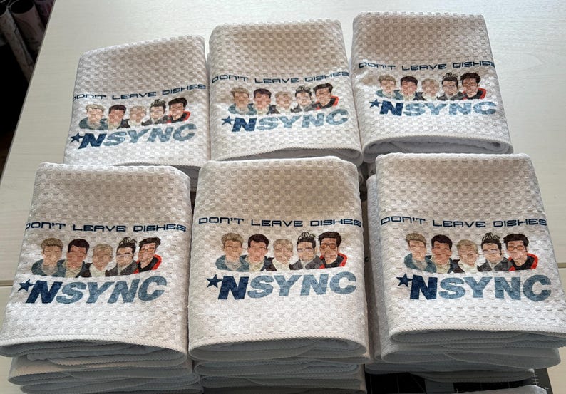 May include: Six white kitchen towels with a blue and white design. The towels feature a group of five cartoon men with the text "Don't Leave Dishes *NSYNC" printed on them.