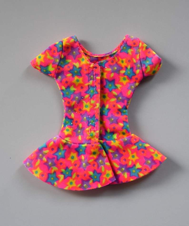 May include: A pink, yellow, blue, and green doll dress with a star print. The dress has short sleeves and a gathered skirt.