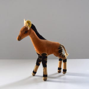 May include: A soft toy giraffe with a tan body and black striped legs and mane. The giraffe has yellow ears and a small, twisted tail. The toy is made of a soft material. The toy is a children's item.