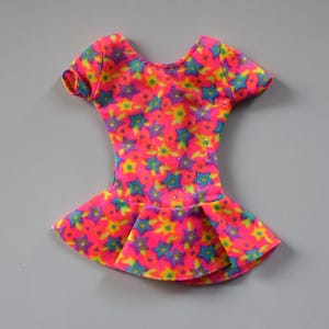 May include: A pink leotard with a multi-colored star print. The leotard has short sleeves and a ruffled skirt.