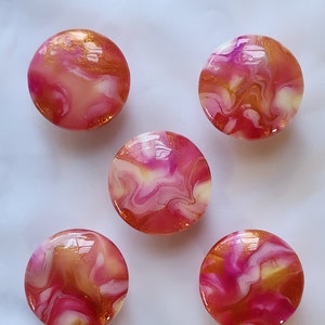 May include: Five round, pink, white, and gold resin cabochons with a marbled swirl pattern.