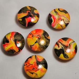 May include: Six round, colorful, abstract, resin, coasters with a marbled design in shades of black, yellow, orange, and pink.