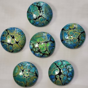 May include: Six round, colorful, abstract, resin coasters with a black, green, blue, and gold color scheme. The coasters have a marbled, swirled, and textured appearance.
