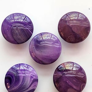 May include: Five circular cabinet knobs featuring a glossy, smooth finish with a marbled pattern in shades of deep purple, lavender, and white. Each knob displays a unique swirling design with reflective highlights across the rounded surface.