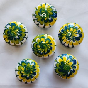 May include: Six round, white candles with a swirling pattern of yellow, green, and blue paint.