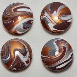 May include: Four round decorative cabinet knobs with a swirled pattern. The colors include shades of brown, copper, gray, and white. The knobs have a glossy finish and are arranged in a square formation.