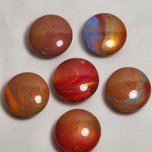 May include: Six round, smooth, colorful, abstract, painted, resin, paperweights with swirling patterns in shades of red, orange, blue, and gold.