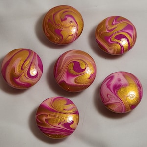 May include: Six round, smooth, pink and gold painted stones with a marbled design.