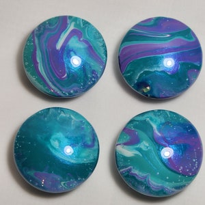 May include: Four round, teal, purple, and white marbled coasters with a glossy finish.