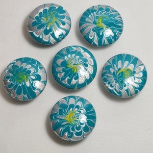 May include: Six round teal blue and silver painted coasters with a swirling pattern. The coasters have a white background with silver and teal blue swirls.