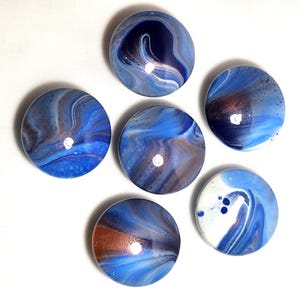May include: Six circular cabochons featuring a glossy, marbled finish with swirling patterns of deep navy blue, bright sky blue, white, and metallic copper tones. Each piece has a smooth, domed surface that reflects light, creating a polished appearance.