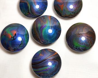 May include: Six circular cabinet knobs featuring a glossy, poured paint finish with swirling patterns of deep blue, vibrant green, bright orange, and purple. Each knob has a smooth, reflective surface with a distinct, unique marbled color blend.