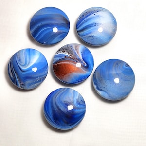 May include: Six circular cabinet knobs featuring a glossy finish with a marbled pattern in shades of blue, white, and copper. Each knob displays a unique fluid acrylic pour design with swirling colors and small dark speckles across the surface.