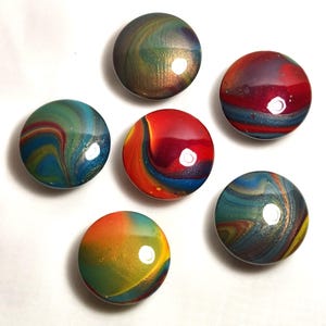 May include: A set of five circular cabinet knobs featuring a glossy, multi-colored swirl pattern. Each knob displays a unique blend of vibrant colors including red, blue, green, yellow, and gold, with a smooth, reflective finish on the surface.