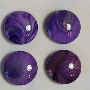 May include: Four round purple and white swirl glass cabochons with a glossy finish.