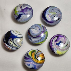 May include: Six round, colorful, abstract, swirl-patterned, glass ornaments. The ornaments are white with blue, purple, green, and gold swirls.