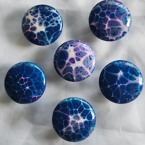 May include: Six round, blue, purple, and white abstract painted ceramic knobs. The knobs have a marbled, swirled, and textured appearance.