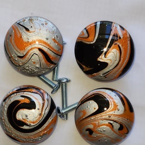May include: Four round, black, silver, and orange marbled cabinet knobs with silver screws.