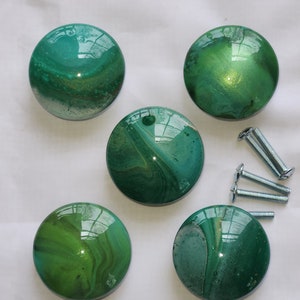 May include: Five green and gold swirl resin cabinet knobs with a glossy finish.