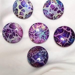 May include: Six circular cabochons featuring a fluid acrylic pour design with a glossy finish. The patterns consist of interconnected organic shapes in shades of deep purple, violet, light blue, and white, creating a marbled effect across each piece.
