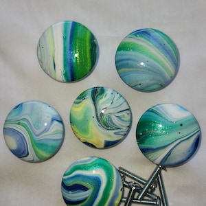 May include: Six round, green, blue, and white marble-like cabinet knobs with a swirl pattern. The knobs are arranged in a circle around a pile of silver screws.