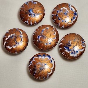 May include: Six round, copper-colored, decorative coasters with a white and blue swirl design.