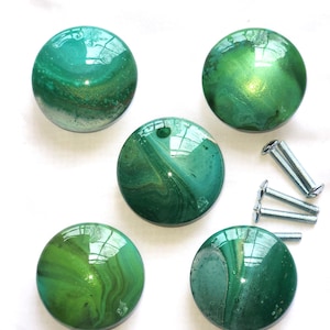 May include: Five circular cabinet knobs with a glossy, marbled finish in shades of emerald, forest green, and lime, featuring swirling patterns and metallic gold accents. Three silver-toned metal mounting screws are included for installation.