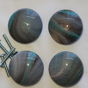 May include: Four round, iridescent, glass cabinet knobs with a swirling pattern of gray, teal, and gold. The knobs have a shiny, metallic finish.