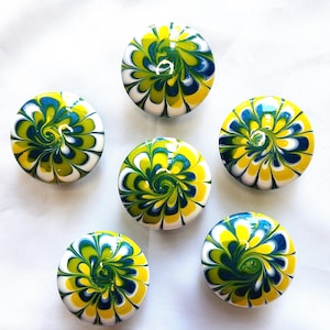 May include: A set of five round, flat candles featuring a marbled swirl pattern in vibrant shades of yellow, lime green, dark blue, and white. Each candle has a small, centered wick visible on the smooth, glossy surface of the wax discs.