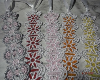 May include: Five white lace bookmarks with different colored floral designs. The bookmarks are made of white lace with a ribbon attached to the top. The floral designs are in shades of pink, red, orange, and yellow.