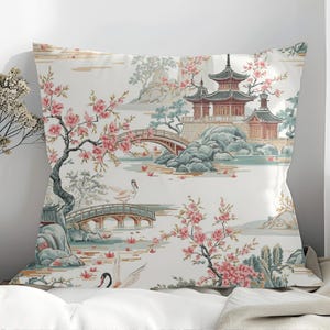 Könnte beinhalten: Dekoratives Kissen mit japanisch inspiriertem Design. Das Kissen zeigt eine ruhige Landschaft mit einer Pagode, Brücken, Kirschblüten und Schwänen in Rosa-, Blau- und Beigetönen. Das Kissen ist rechteckig.