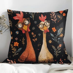 Op de afbeelding: Decoratief vierkant kussen met twee grillige kippen met een bril op een zwarte achtergrond. De kippen zijn in bruin- en crèmetinten, met rode kammen en gele snavels. Het kussen is versierd met bloemen en botanische elementen in oranje, blauw en groen.