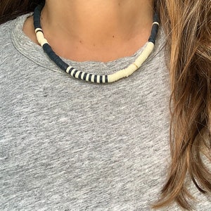 May include: A black and white beaded necklace with a gold accent. The necklace is made of round beads and is worn by a person with long brown hair.