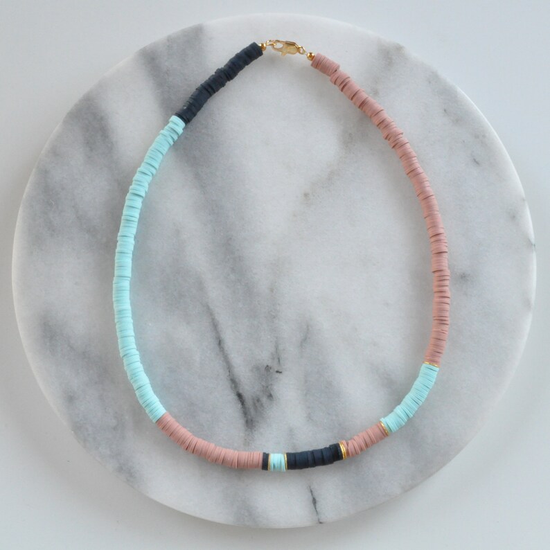 May include: A necklace made of light blue, pink, and black ceramic beads with a gold clasp.