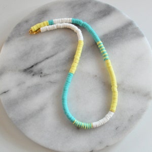 May include: A colorful necklace made of white, yellow, and turquoise beads. The necklace is made of a series of stacked beads, creating a unique and eye-catching design.