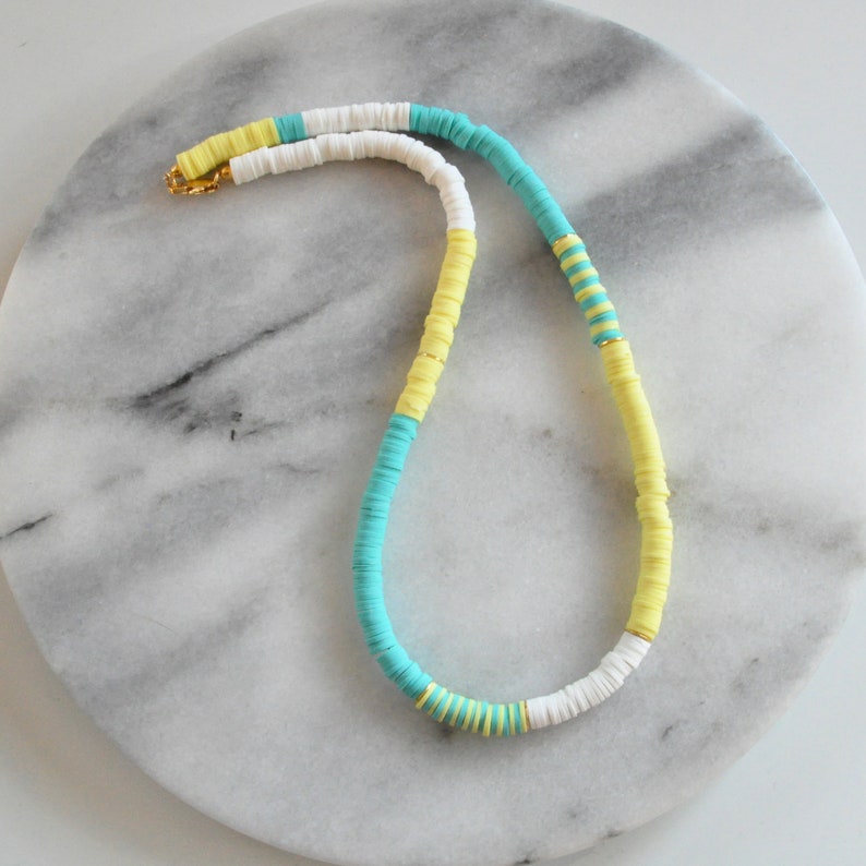 May include: A colorful necklace made of white, yellow, and turquoise beads. The necklace is made of a series of stacked beads, creating a unique and eye-catching design.