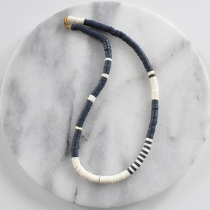 May include: A black and white beaded necklace with gold accents. The necklace is made of flat, round beads and is arranged in a striped pattern.