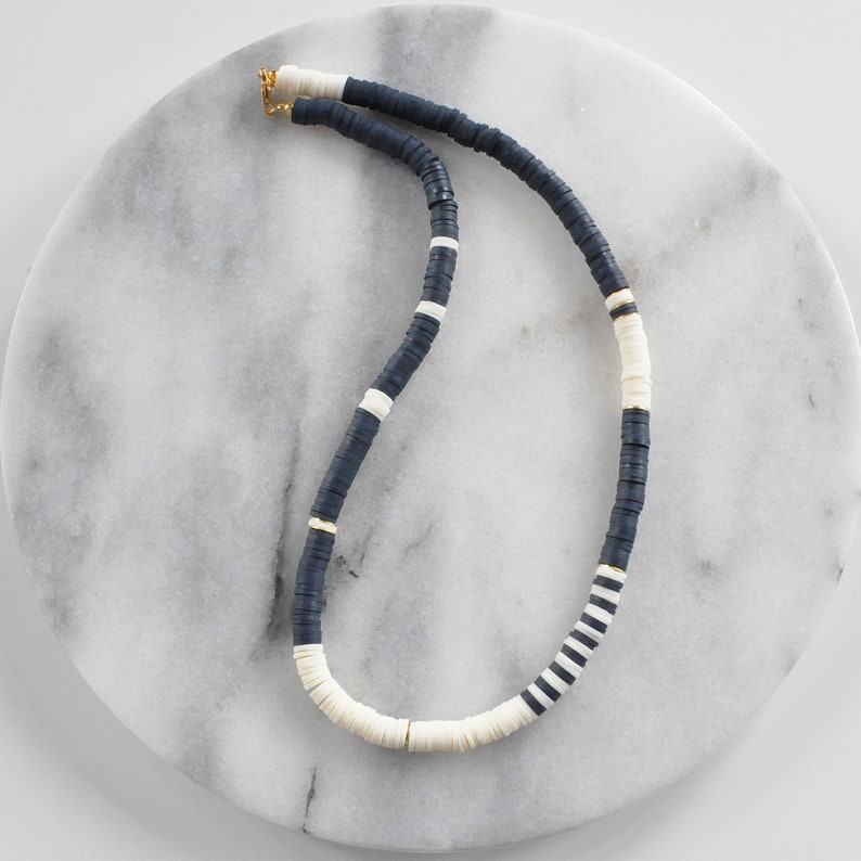 May include: A black and white beaded necklace with gold accents. The necklace is made of flat, round beads and is arranged in a striped pattern.