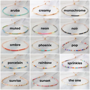 May include: A collection of 15 colorful beaded bracelets with adjustable string closures. Each bracelet has a unique name, such as "aruba", "creamy", "monochrome", "muted", "neon", "noir", "ombre", "phoenix", "pop", "porcelain", "rainbow", "sprinkles", "sunrise", "sunset", and "the one".
