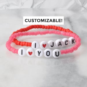 May include: Two beaded bracelets with the words "I love you" and "I love Jack" spelled out in white beads with black lettering. The bracelets are pink and red.